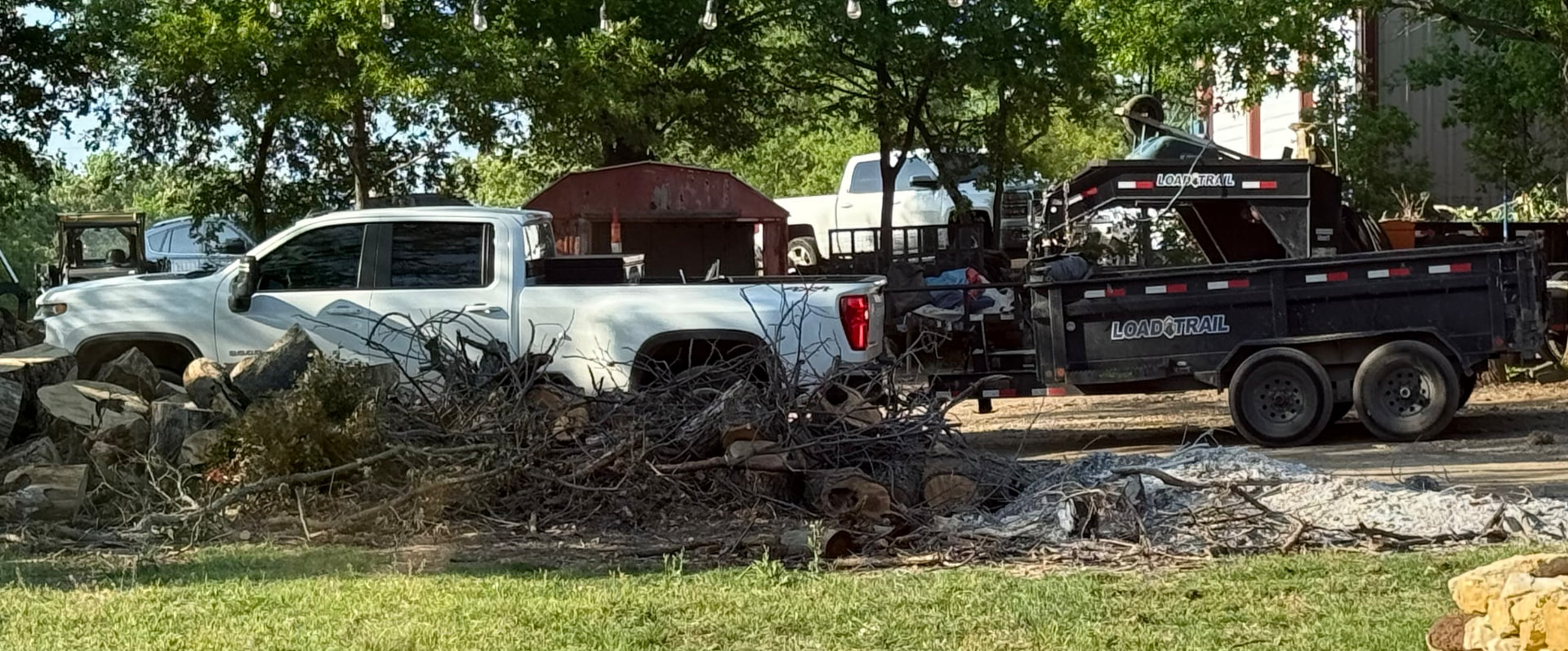 D&A Haul Away white pickup truck and black dump trailer on a job site with yard debris ready for removal